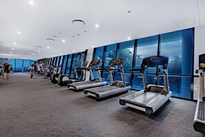 Une salle de sport moderne avec des tapis de course alignés le long d’un mur doté de grandes fenêtres.
