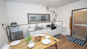 A compact kitchen with a microwave, stove, sink, and a window. There is a dining table with plates, bowls, and utensils. - Ra Villa Hanazono (Osaka)