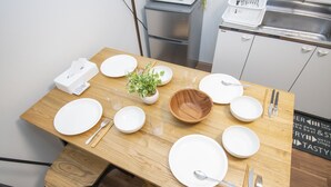 A dining table set with white plates, bowls, and cutlery, a small potted plant, and a remote control. - Ra Villa Hanazono (Osaka)
