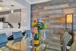 Ett modernt matområde med ett glasbord, blå stolar, en blomsterdekoration i mitten av bordet och en flaska Veuve Clicquot Brut-champagne.