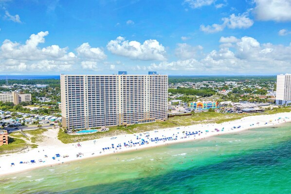 A beachfront hotel with multiple floors, a pool, and a beach with umbrellas.