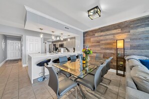 Eine moderne Küche mit Kochinsel, Essbereich mit Glastisch und Stühlen sowie ein gemütlicher Wohnbereich mit Sofa und Lampe.