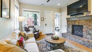 A living room with a fireplace, a ceiling fan, a flat-screen TV, and a large window. - Hot Tub + Fire Pit: Modern Flagstaff Home (Flagstaff)