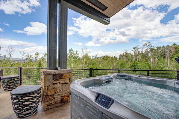 Un jacuzzi con panel de control, rodeado de barandillas de piedra y metal, con vistas a un paisaje boscoso.