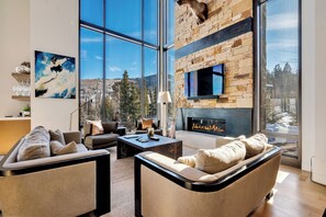 Una sala de estar moderna con chimenea de piedra, ventanas amplias y vistas a la montaña.