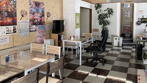 A hotel lobby with a checkered floor, wooden tables, black office chairs, a TV on a stand, and various posters on the walls. - Hostel Hirosaki - Hostel (Hirosaki)