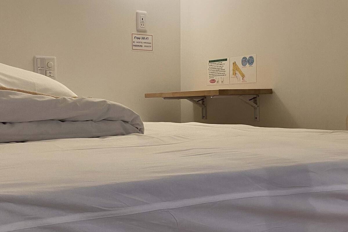 En snyggt bäddad säng med vita sängkläder i ett hotellrum. Bredvid sängen står ett litet träbord med en skylt som visar att det finns gratis Wi-Fi.