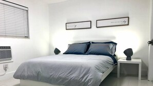 A modern bedroom with a bed, two bedside tables, a wall-mounted air conditioner, and two framed pictures. - THE GROVE 6    10 MIN FROM THE BEACH In the heart of Coconut Grove and CocoWalk (Miami)