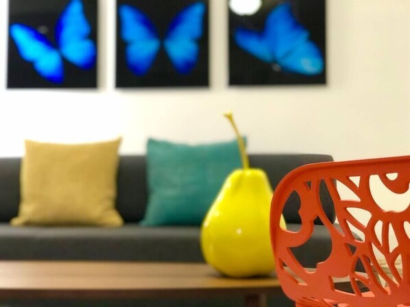 A living room with a sofa, cushions, a yellow vase, and a red chair.