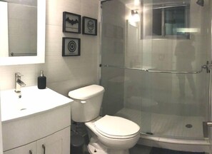 A bathroom with a white sink, a toilet, and a glass-enclosed shower. There are framed pictures on the wall.