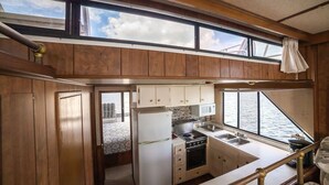 A compact kitchen with wooden cabinets, a refrigerator, stove, and a sink. - Happy’s Houseboat Key West (Key West)