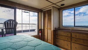 A room with a bed, a wooden dresser, a chair, and a window overlooking a body of water. - Happy’s Houseboat Key West (Key West)
