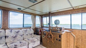 A cabin with a wooden interior, large windows, a captain's wheel, and a sofa. - Happy’s Houseboat Key West (Key West)