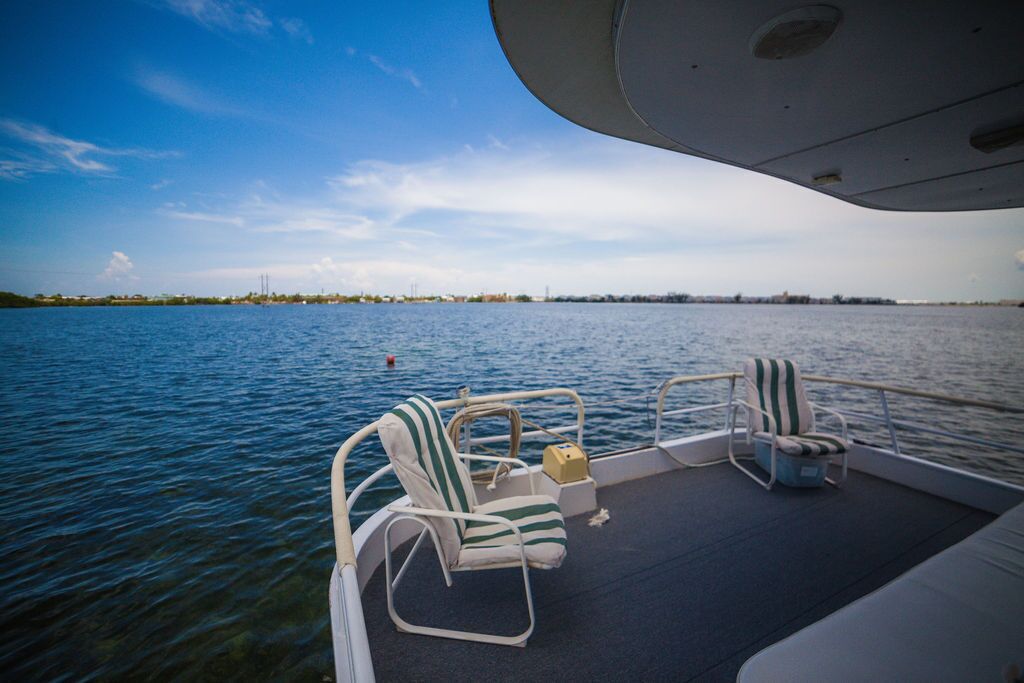 Een scheepsdek met twee gestreepte loungestoelen, een tafeltje en uitzicht op het water en de verre kustlijn.