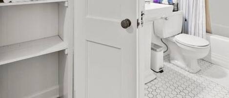 A bathroom with a white door, a toilet, a sink, and a shower area.