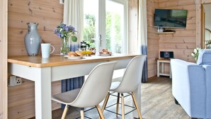 A wooden cabin interior with a breakfast setup on a wooden table, two chairs, a TV, and a sofa. - Cutterbrough, Great Field Lodges -  a lodge that sleeps 2 guests  in 1 bedroom (Braunton)