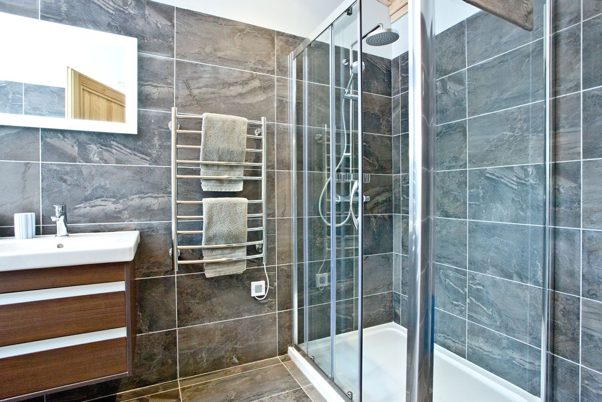 A modern bathroom with a glass-enclosed shower, a glass-enclosed bathtub, and a wooden vanity with a mirror.