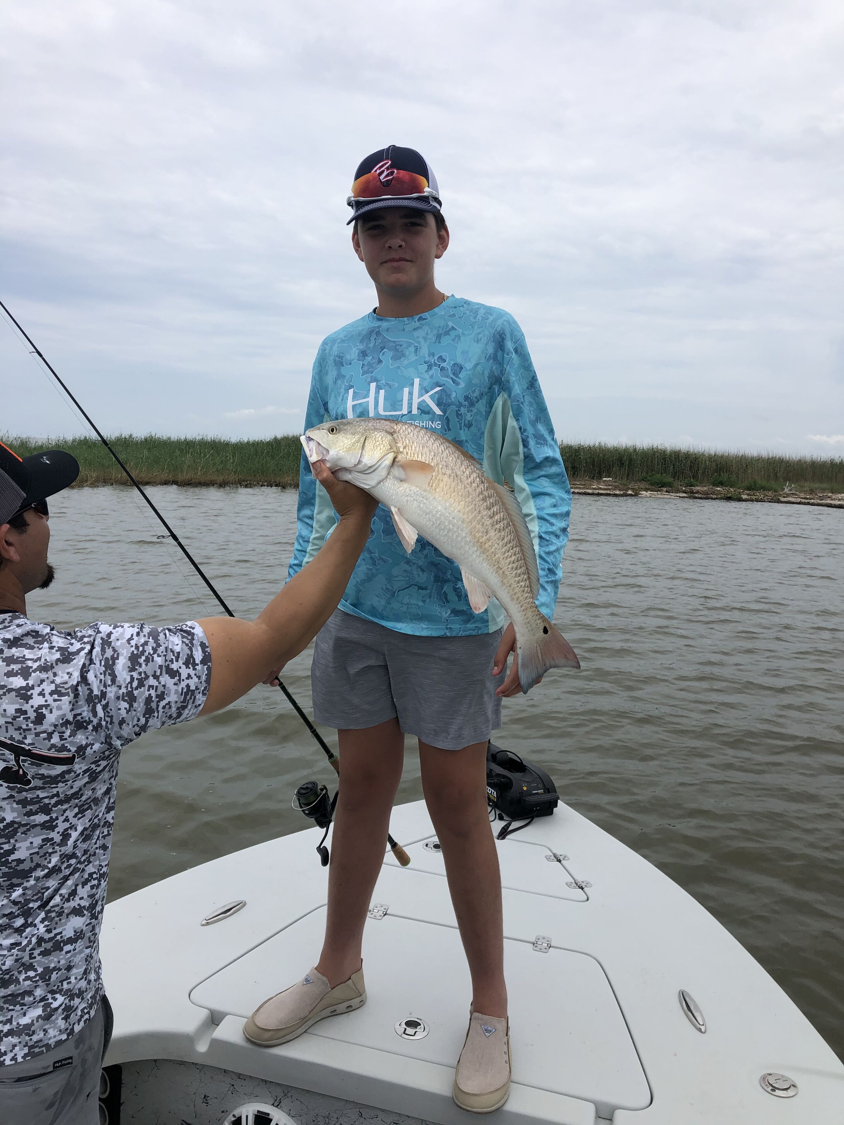 Une personne tenant un poisson sur un bateau, avec une canne à pêche.