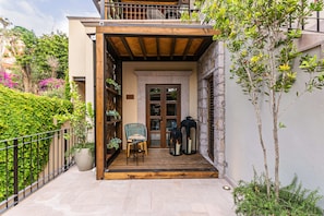A wooden balcony with a chair and a table, surrounded by greenery and a stone wall. - Hotel Apapacho Boutique (San Miguel de Allende)