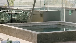 Un espace piscine sur le toit, avec des chaises longues, un jacuzzi à ciel ouvert et une vue sur le paysage urbain.