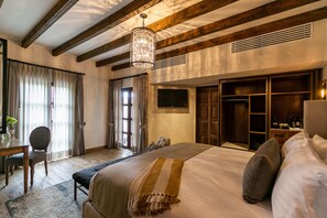 Quarto com uma cama grande, vigas de madeira, um candelabro, uma TV e um guarda-roupa.