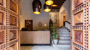 Un espace d’accueil doté d’un comptoir de réception en bois, d’un mur orné de motifs et d’un escalier agrémenté d’une décoration murale.