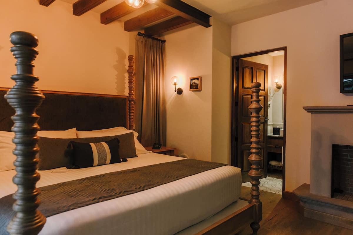 Une chambre à coucher avec un lit à baldaquin, une table de chevet, une lampe fixée au mur et une cheminée.