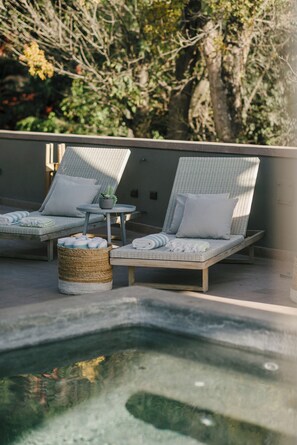 Uma área ao lado da piscina com duas espreguiçadeiras, uma mesinha com uma planta em vaso e uma cesta de vime.