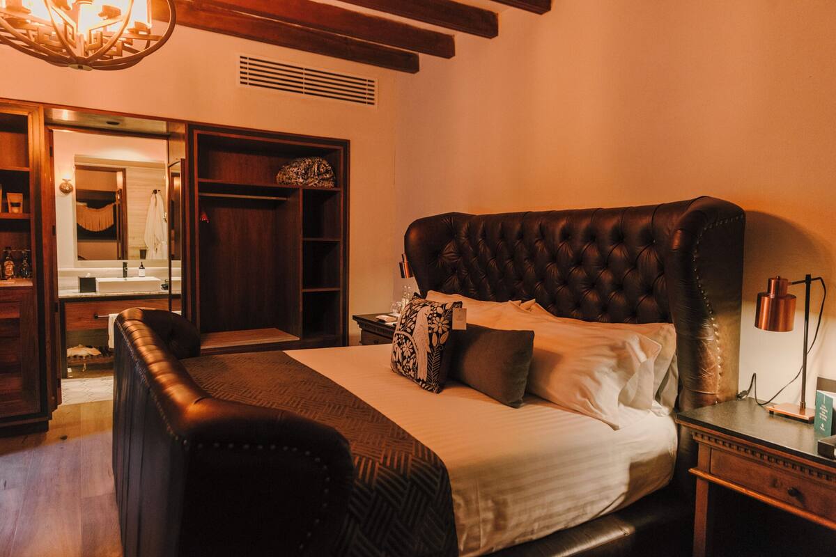 Une chambre à coucher avec un grand lit, une armoire en bois, un miroir et une table de chevet avec une lampe.