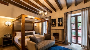 Un lit à baldaquin avec un cadre en bois, un canapé, une cheminée et une grande fenêtre avec des rideaux.