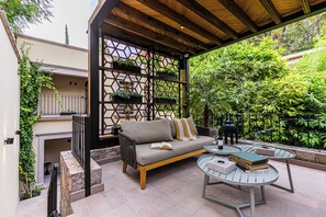 A covered outdoor seating area with a sofa, two round tables, and a decorative wall with planters. - Hotel Apapacho Boutique (San Miguel de Allende)