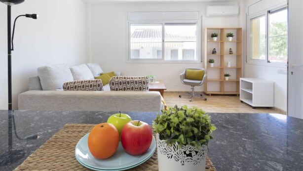 Ein modernes Wohnzimmer mit einer Couch, einem Couchtisch mit Früchten, einem Sessel und einem Bücherregal.