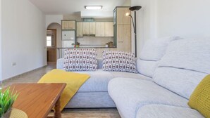 Ein modernes Wohnzimmer mit einer Couch, einem Holztisch und einer Küche im Hintergrund.