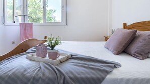 Ein Schlafzimmer mit Bett, Fenster, Nachttisch und Tablett mit Tasse und Pflanze.