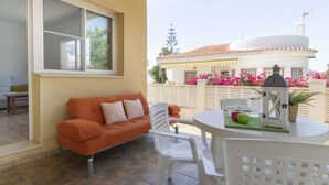 Ein Balkon mit einem weißen Tisch, einem orangenen Sofa und Blick auf ein weißes Gebäude mit rosa Blumen.