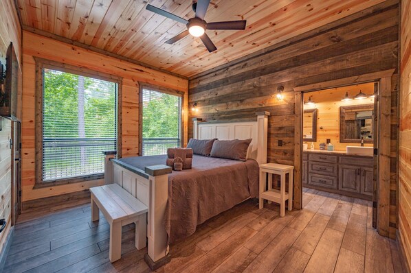Interior de una cabaña de madera con cama, banco y pequeña cocina.