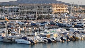 Una marina con numerose imbarcazioni ormeggiate, un’area parcheggio con auto e un complesso di edifici sullo sfondo.