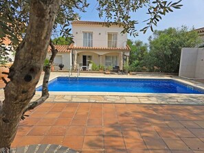 A two-story building with a swimming pool, surrounded by a tiled patio and greenery.