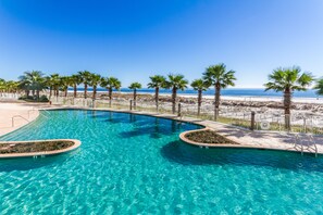 Une piscine à l’eau cristalline, entourée de palmiers et bordée d’une plage de sable.