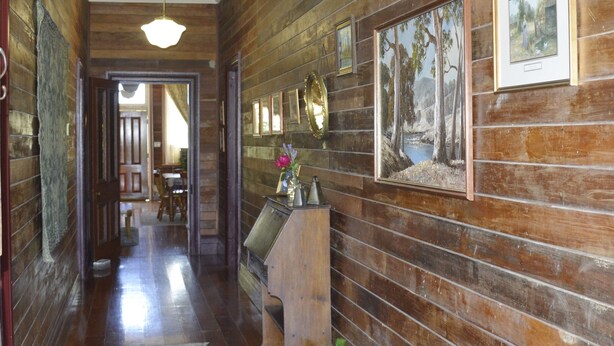 Un couloir en bois, agrémenté d’un tapis, de tableaux encadrés et d’un petit autel sur lequel sont posés un vase et une plante.