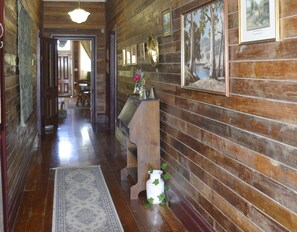 A wooden hallway with a rug, framed pictures, and a small altar with a vase and plant.