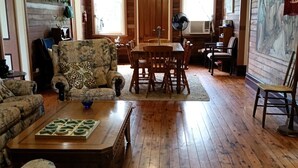 Un salon chaleureux avec un parquet, un canapé à motifs floraux, une table basse en bois et un coin repas comprenant une table et des chaises en bois.