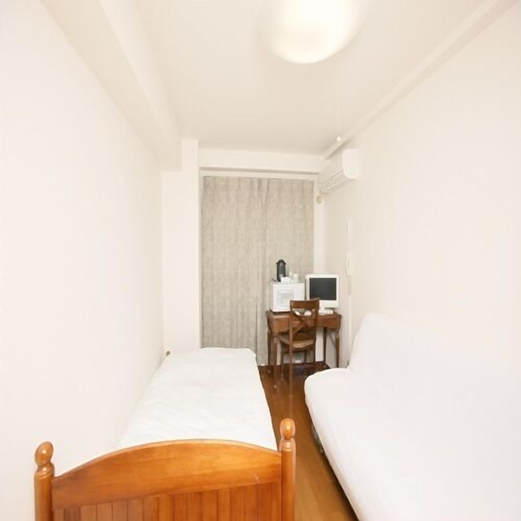 A narrow room with two single beds, a desk with a computer, and a chair.