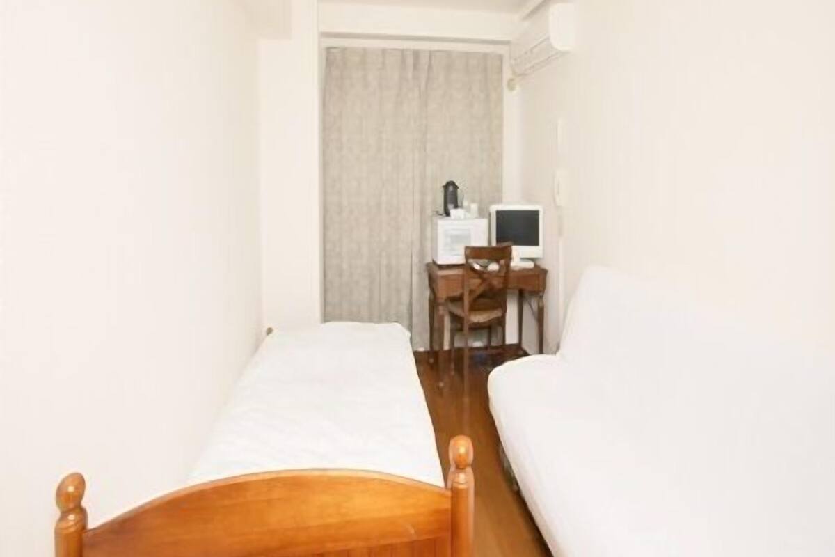 A narrow room with two single beds, a desk with a computer, and a chair.
