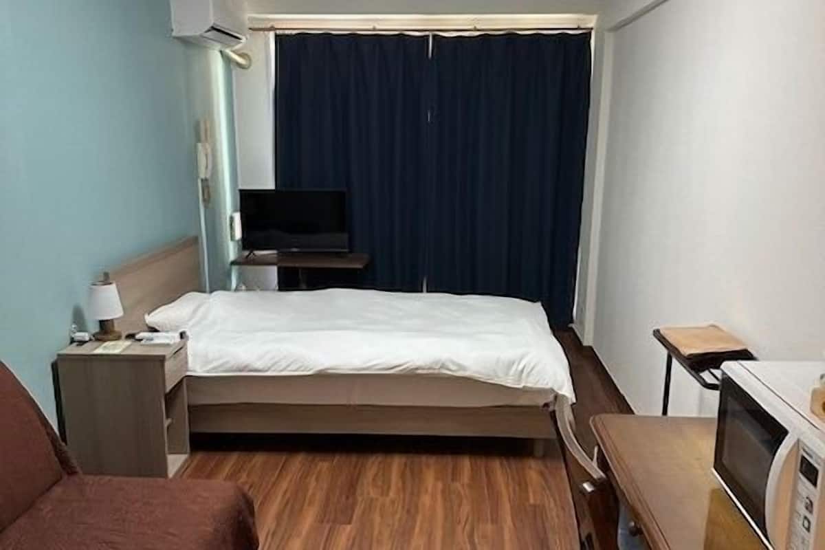 Hotellihuone, jossa on sänky, työpöytä, tuoli, televisio ja mikroaaltouuni.