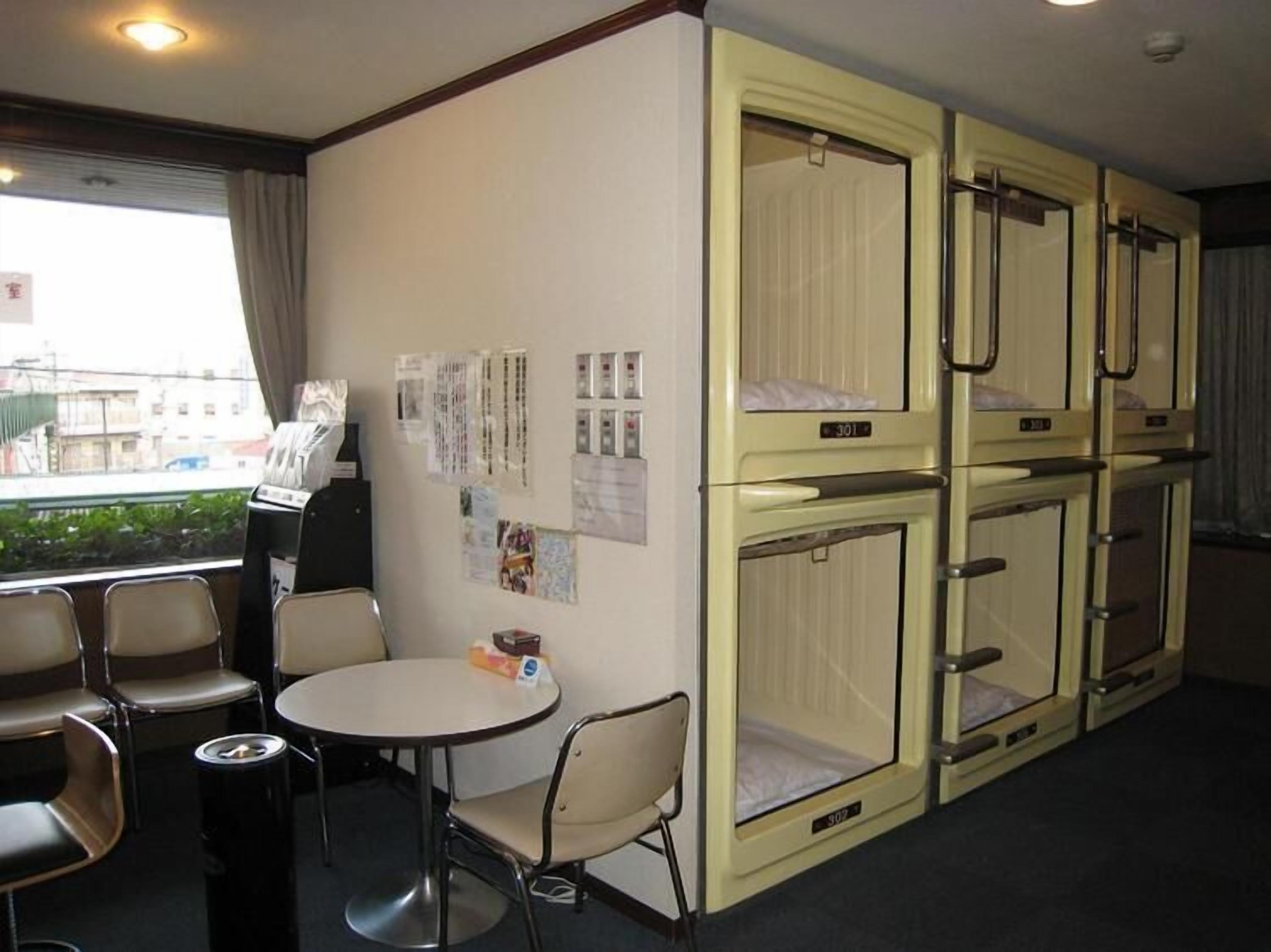 A hotel room with bunk beds, a small table with chairs, and a window with a view of buildings.