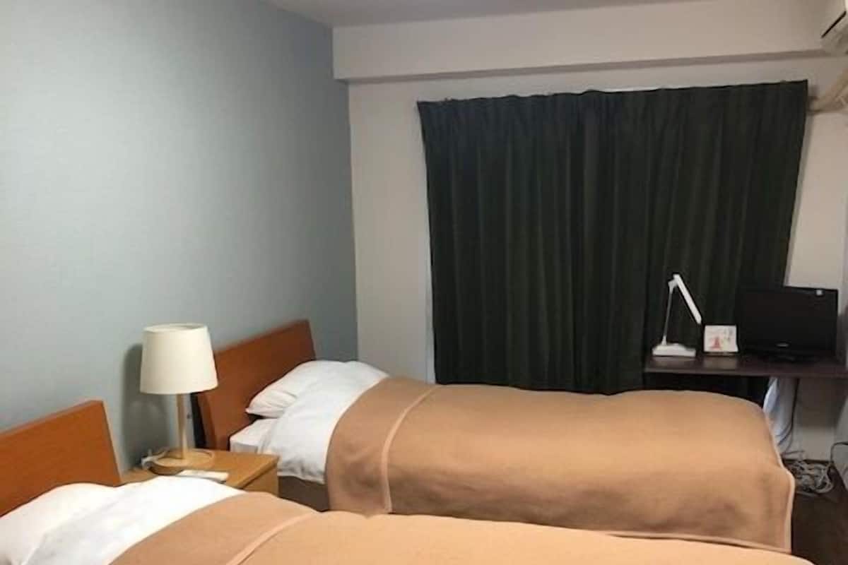 A hotel room with two beds, a desk, a lamp, a TV, and a curtain.