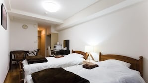 A hotel room with two beds, a desk, a chair, a lamp, and a clock on the wall. - Hotel Hill top (Tokyo)