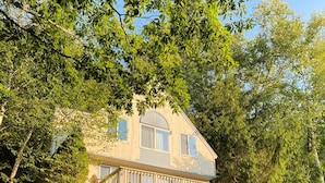 Une maison à deux étages avec un balcon, entourée d’arbres et bordée d’un chemin de gravier.