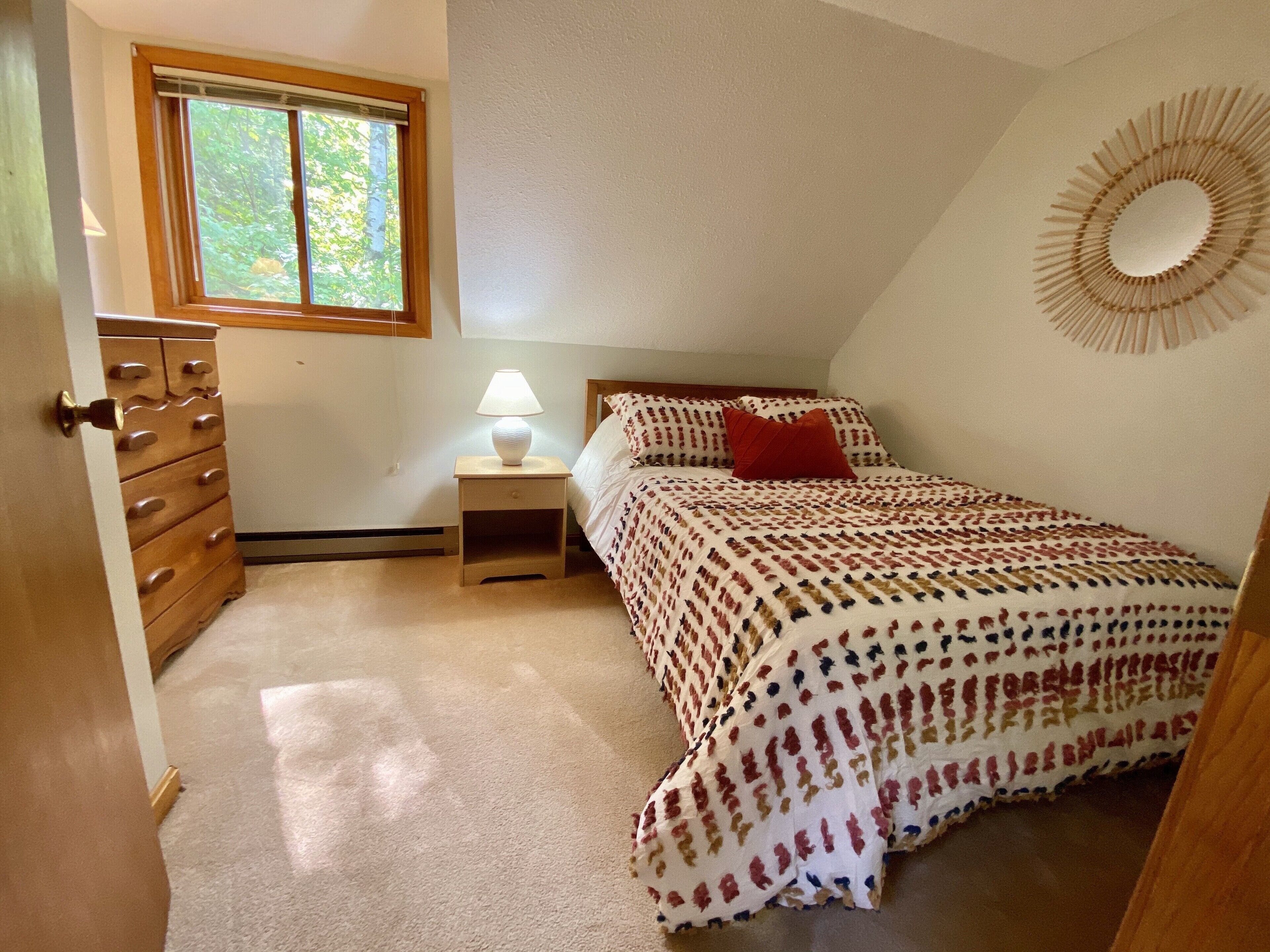 Une chambre à coucher comprenant un lit, une commode, une table de chevet, une fenêtre et un élément décoratif mural.